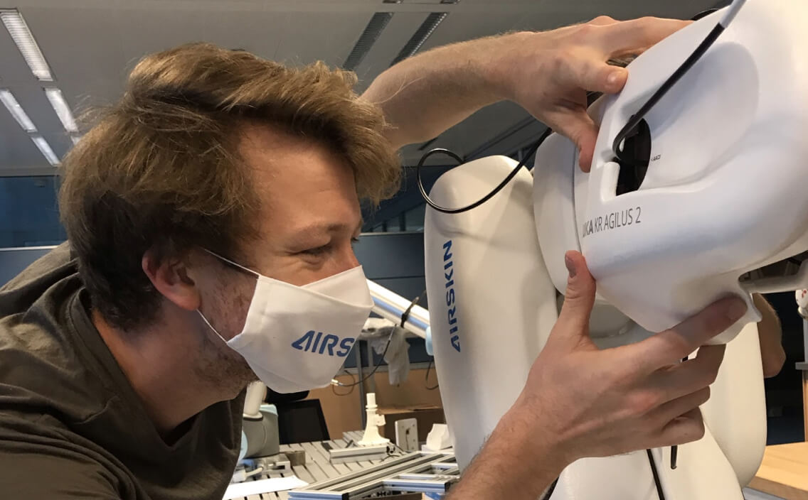 young man taking a close look at the agilus 2 collaborative robot covered with AIRSKIN